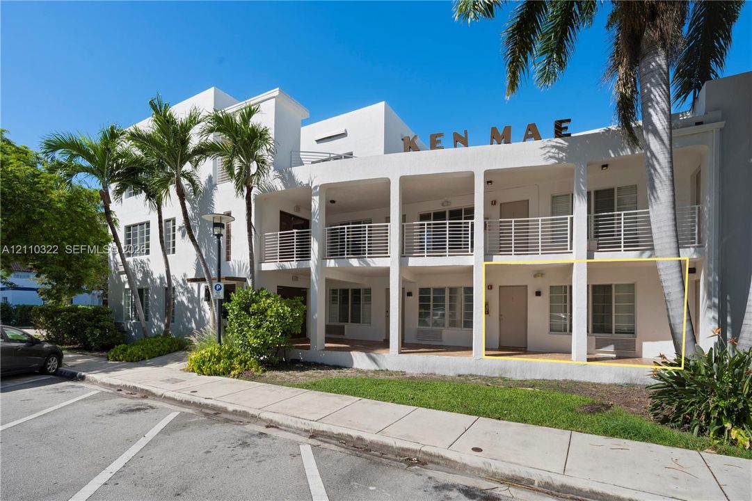 Multi-story building facade with stucco exterior, ground-level covered patio, and metal railings