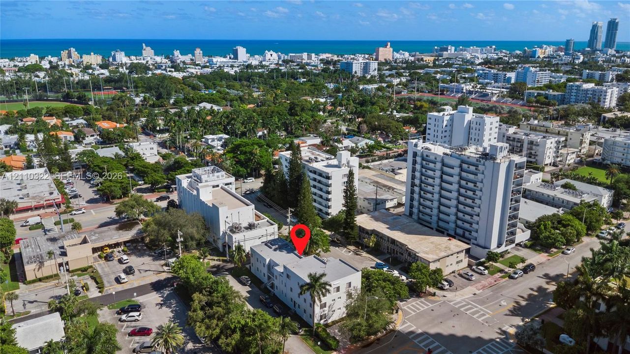 Aerial perspective of a multi-story building featuring a flat roof and ground-level surface parking, situated within a coastal urban environment