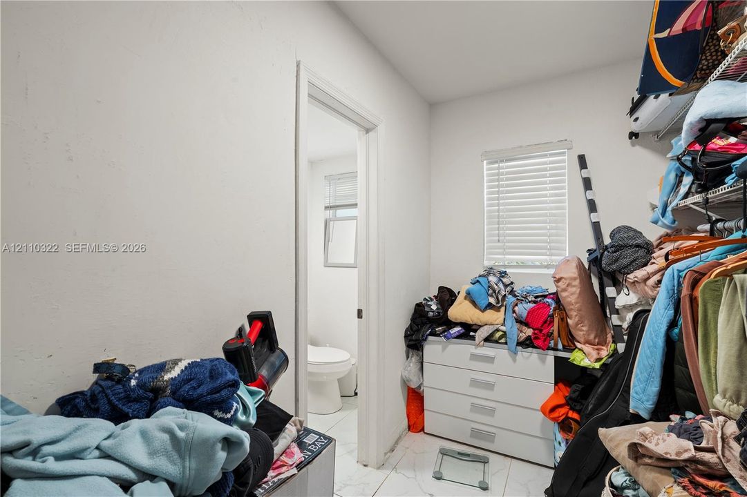 Storage room featuring white built-in cabinetry, wire shelving, tile flooring, and a window with horizontal blinds
