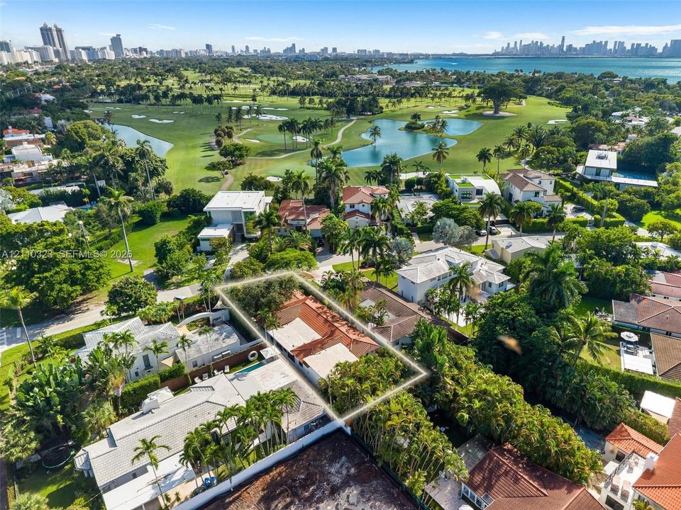 Aerial perspective highlighting a property with a clay tile roof, mature perimeter landscaping, and proximity to a golf course, water bodies, and coastal city skyline