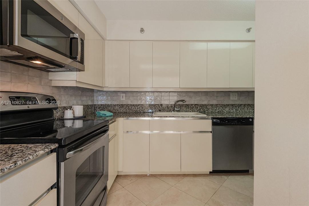 Kitchen featuring glossy flat-panel cabinetry, stone countertops, stainless steel appliances, a tile backsplash, and ceramic floor tiling
