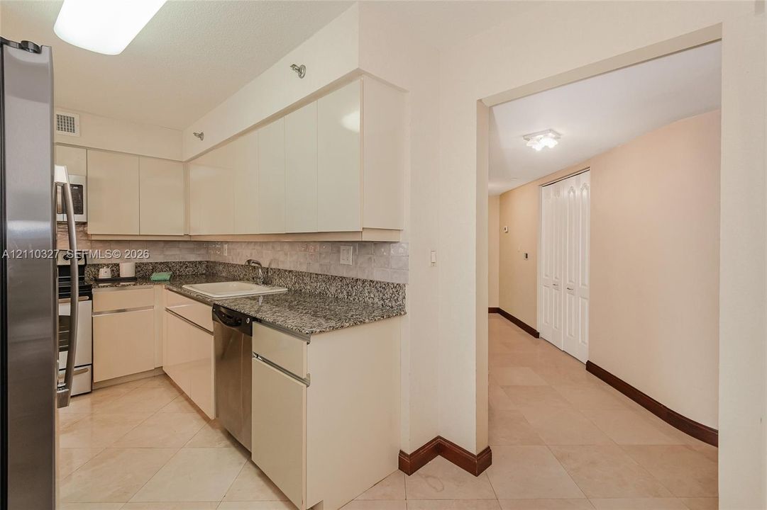Kitchen featuring light-toned cabinetry, stone-finish countertops, stainless steel appliances, tile backsplash, and tile flooring