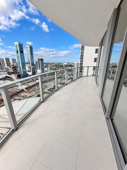 Covered private balcony featuring large-format tile flooring, a glass-panel railing, and floor-to-ceiling glass sliding doors