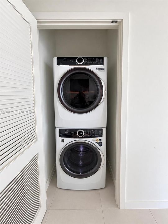 Stacked laundry center featuring a high-efficiency front-load washer and dryer set, housed within a closet with louvered bi-fold doors