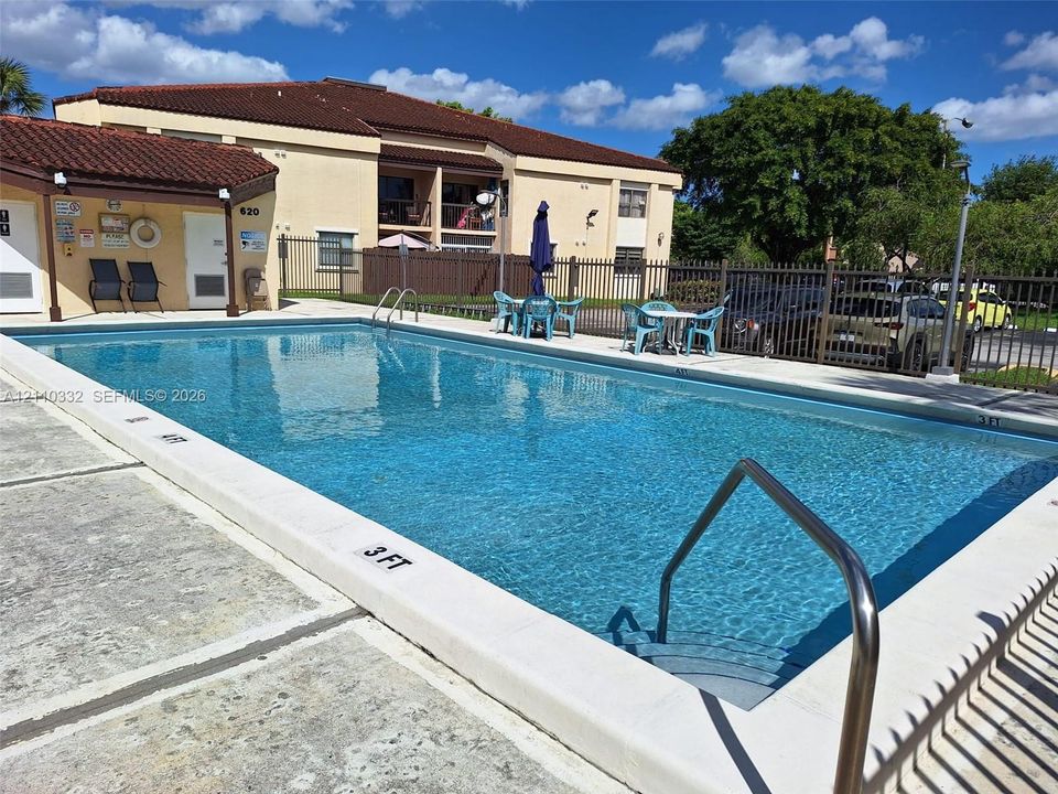 Outdoor swimming pool featuring a concrete deck, metal perimeter fencing, and built-in ladder entry