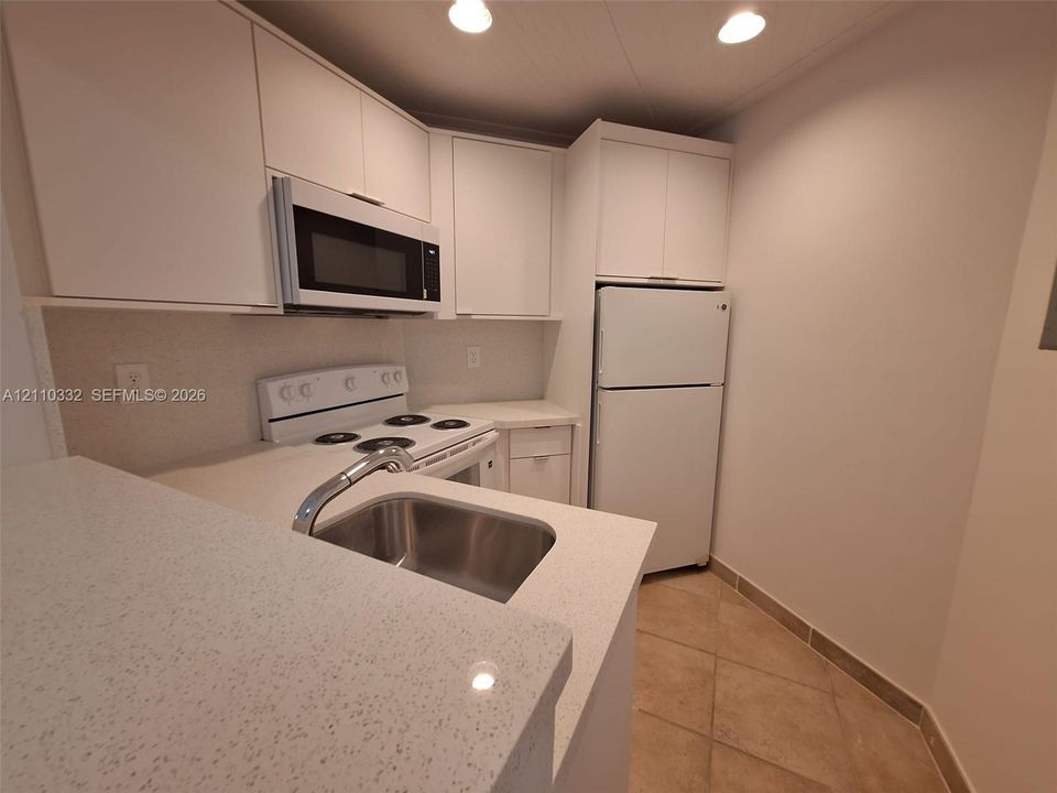 Kitchen featuring white cabinetry, solid-surface countertops, recessed lighting, tile flooring, and integrated white appliances