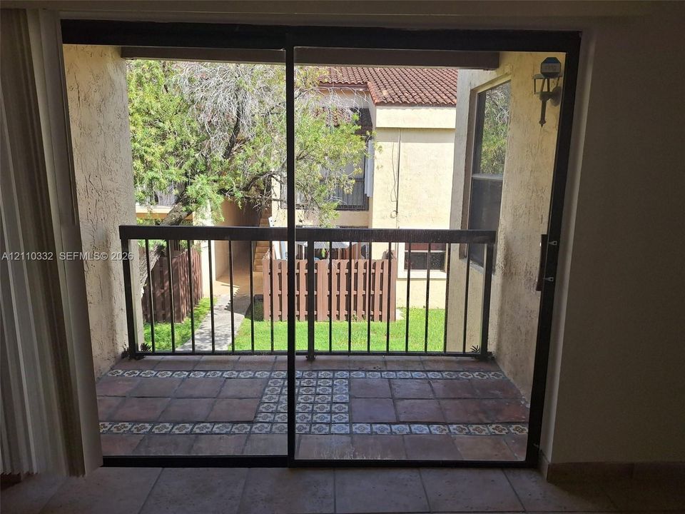 Balcony featuring terracotta-style tile flooring with decorative inlay, dark metal railing, sliding glass door entry, and wall-mounted exterior light fixture
