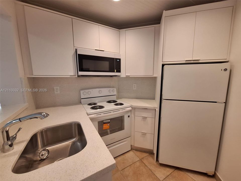 Kitchen featuring white flat-panel cabinetry, quartz countertops, an integrated stainless steel sink with a high-arch pull-down faucet, and white appliances