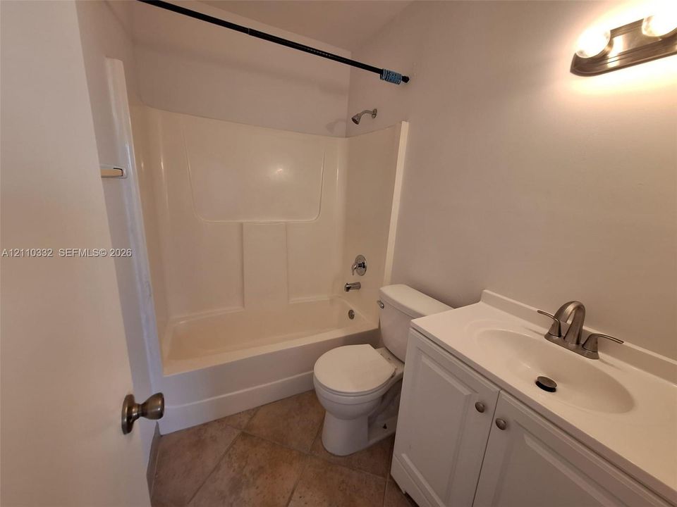 Bathroom featuring tile flooring, a composite tub and shower combination, a white vanity with an integrated sink, and a wall-mounted light fixture