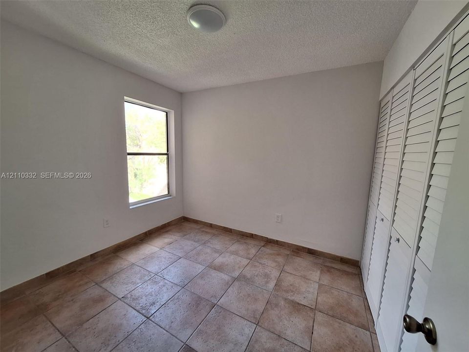 Neutral-toned ceramic tile flooring, built-in louvered-style closet doors, and a single-pane window with natural light exposure