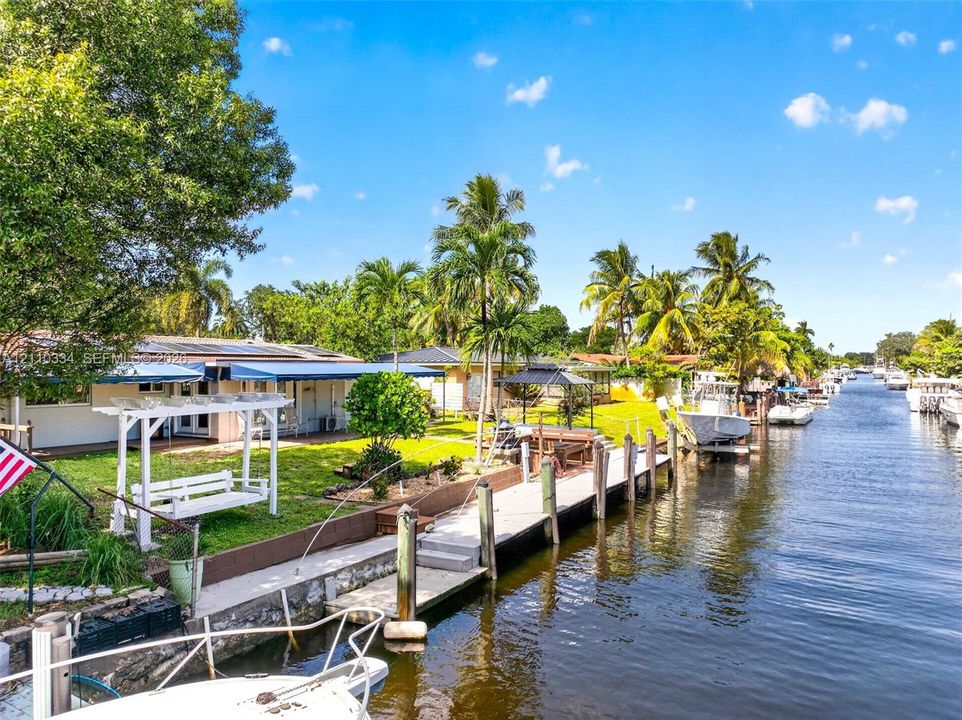 Waterfront property featuring a private concrete boat dock, seawall, landscaped lawn, and retractable exterior awnings