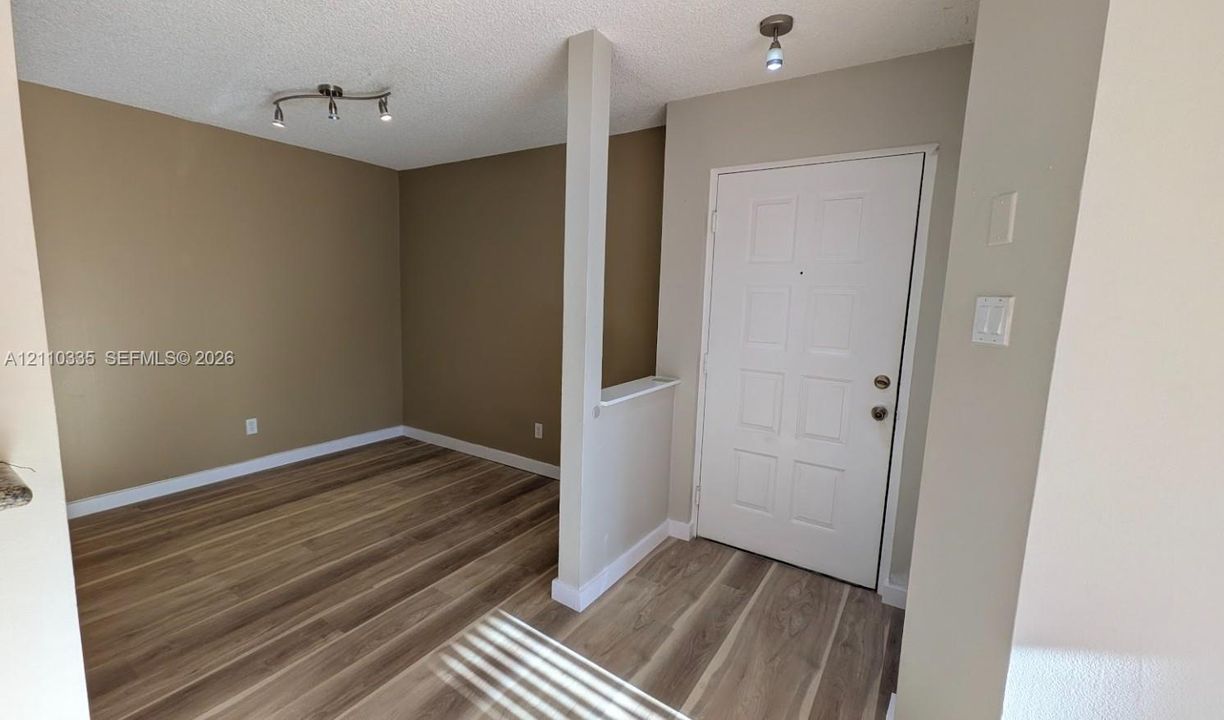 Entryway featuring wood-finish flooring, a paneled door, a structural partition wall with a flat cap, and dual ceiling-mounted track lighting