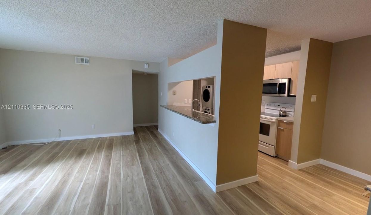 Open-concept interior featuring light wood-finish flooring, a pass-through breakfast bar with stone-surfaced countertop, built-in cabinetry, and a stacked laundry unit