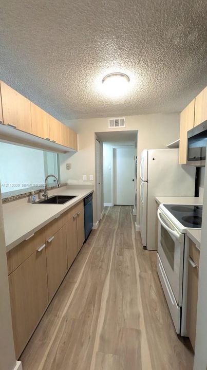 Galley kitchen featuring light-tone cabinetry, wood-finish flooring, solid surface countertops, an undermount sink with a gooseneck faucet, and an over-the-range microwave