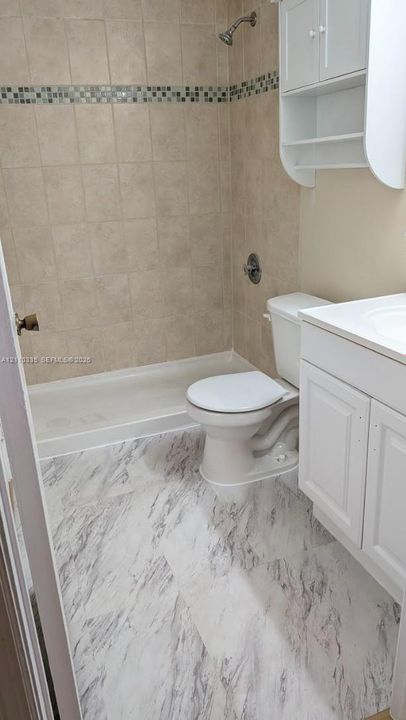 Bathroom featuring a walk-in shower with tile surround, decorative tile inlay, stone-patterned flooring, white vanity cabinet with integrated sink, and white wall-mounted storage cabinetry