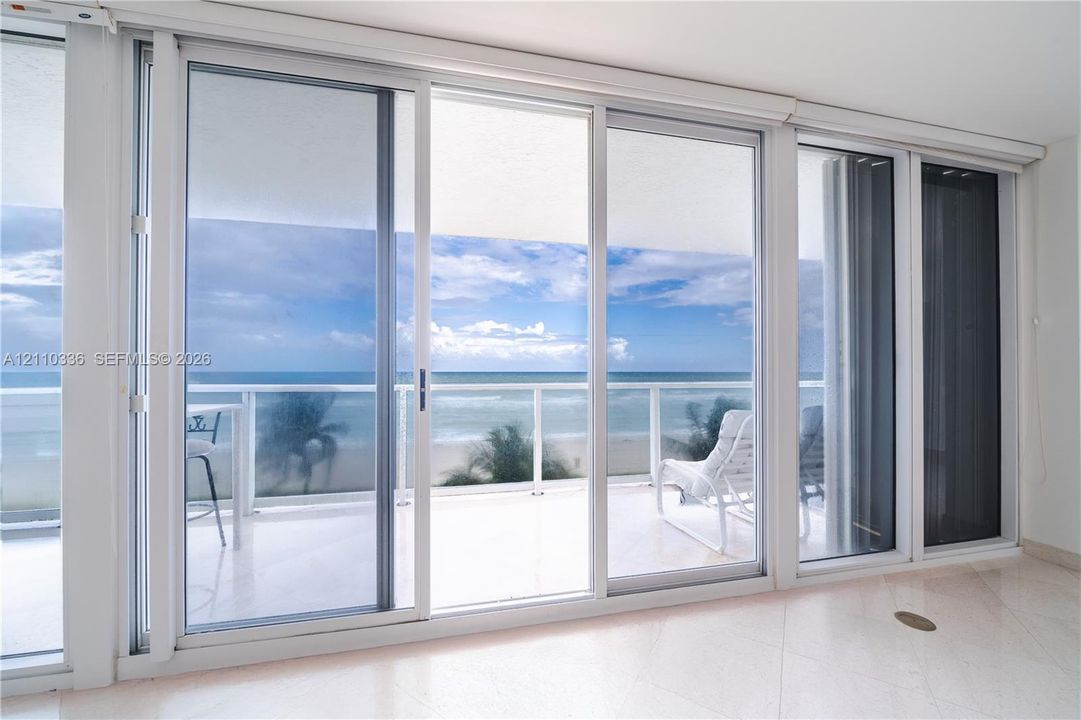 Floor-to-ceiling sliding glass panels, balcony with glass railing, stone flooring, and expansive ocean scenery