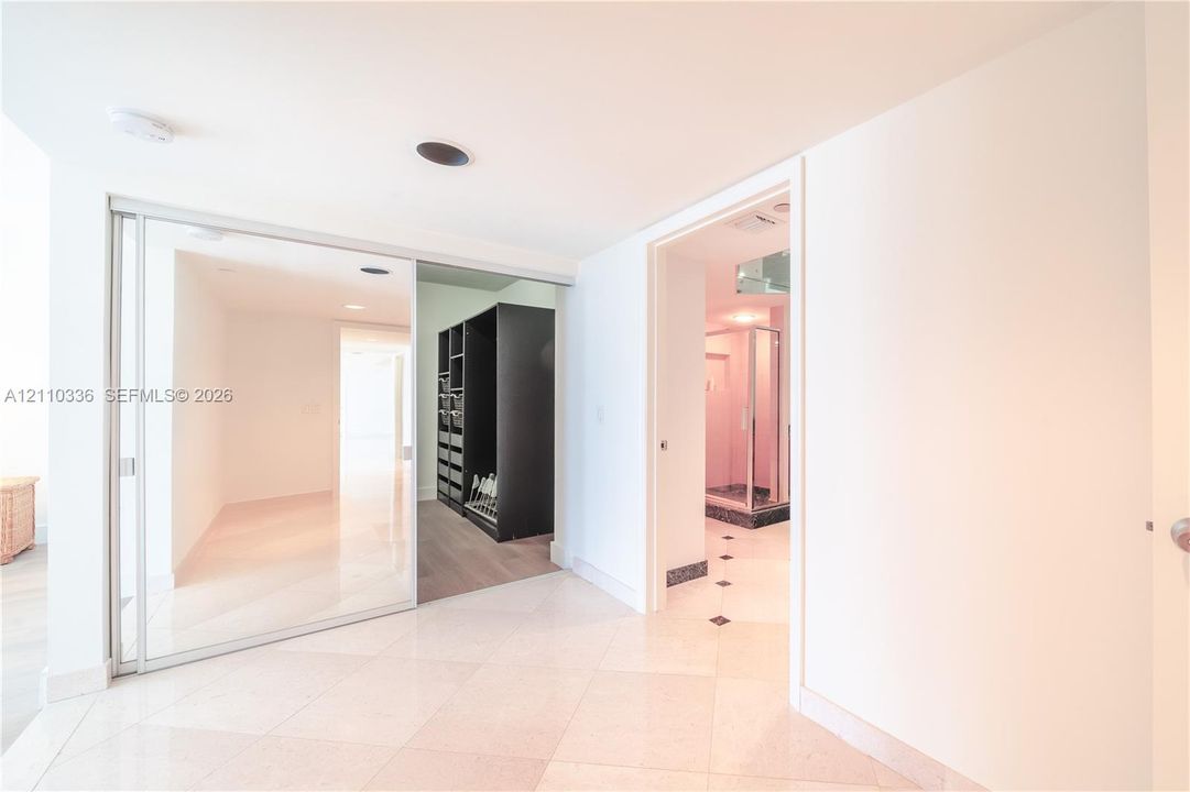 Sliding glass-paneled closet doors, neutral stone-finish tile flooring, recessed ceiling lighting, and built-in closet shelving system