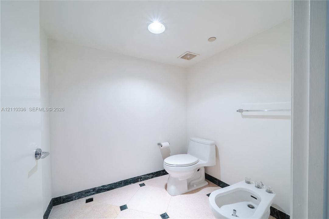 Restroom featuring a dual-piece toilet, porcelain bidet, stone-finish tile flooring with inlaid accents, and a coordinating stone baseboard