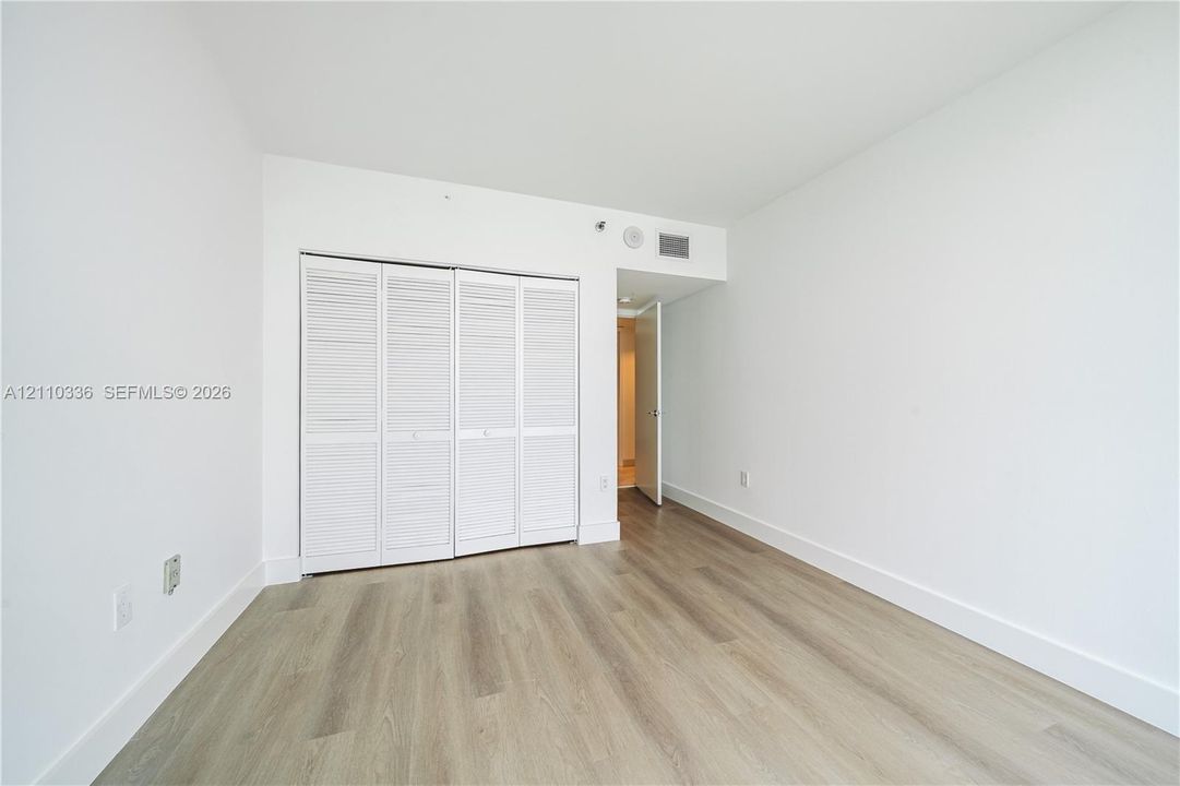Room featuring wood-finish flooring, white walls, and a closet with bifold louvered doors