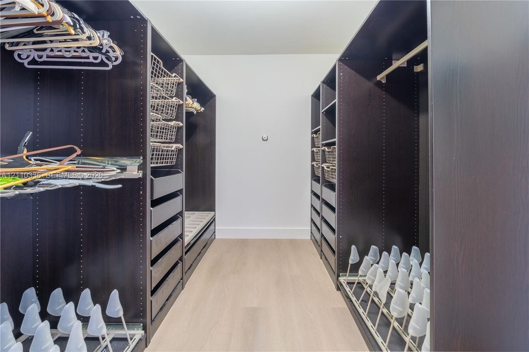 Custom closet featuring dark wood-finish cabinetry, built-in drawer units, integrated wire shelving, and slide-out shoe storage racks