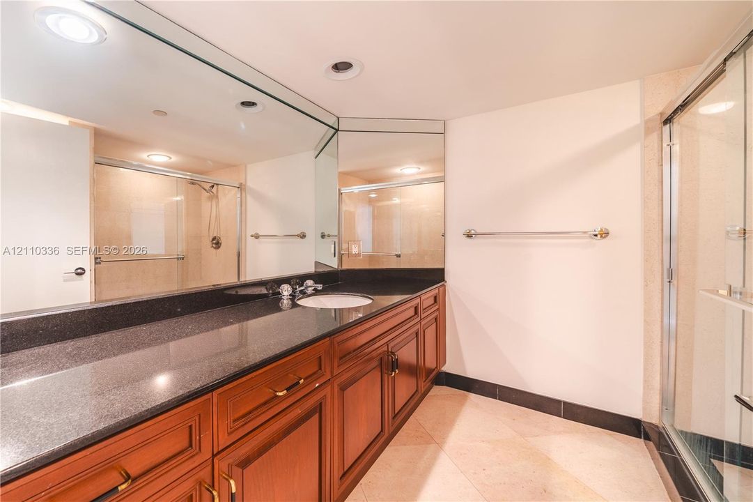 Full-width vanity featuring dark stone-finish countertop, undermount sink, recessed lighting, expansive wall-to-wall mirror, and wood-finish cabinetry