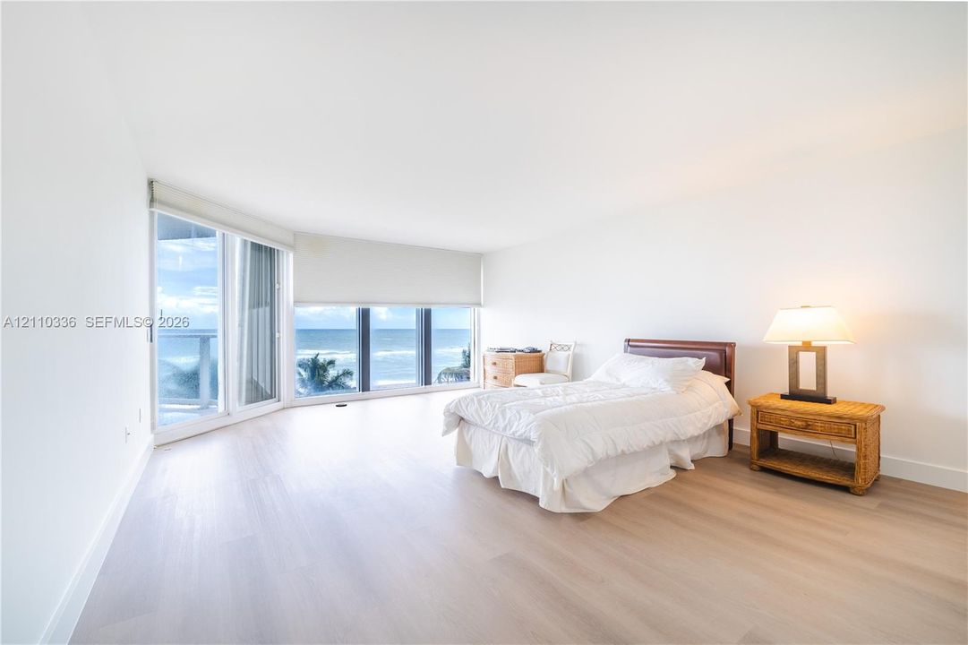Expansive living area featuring floor-to-ceiling windows, light-toned wood-finish flooring, and an oceanic backdrop