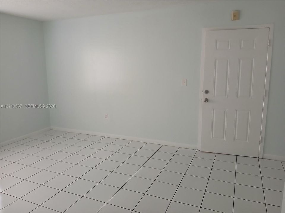 Interior room featuring large-format square tile flooring, neutral wall paint, and a six-panel entry door with metallic hardware