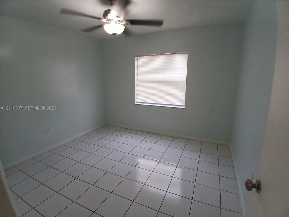 Interior room featuring white tile flooring, neutral wall paint, and a ceiling-mounted light fixture with an integrated fan