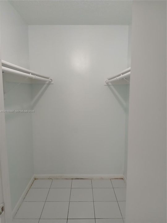 Reach-in storage area featuring white tile flooring and dual-level hanging rods