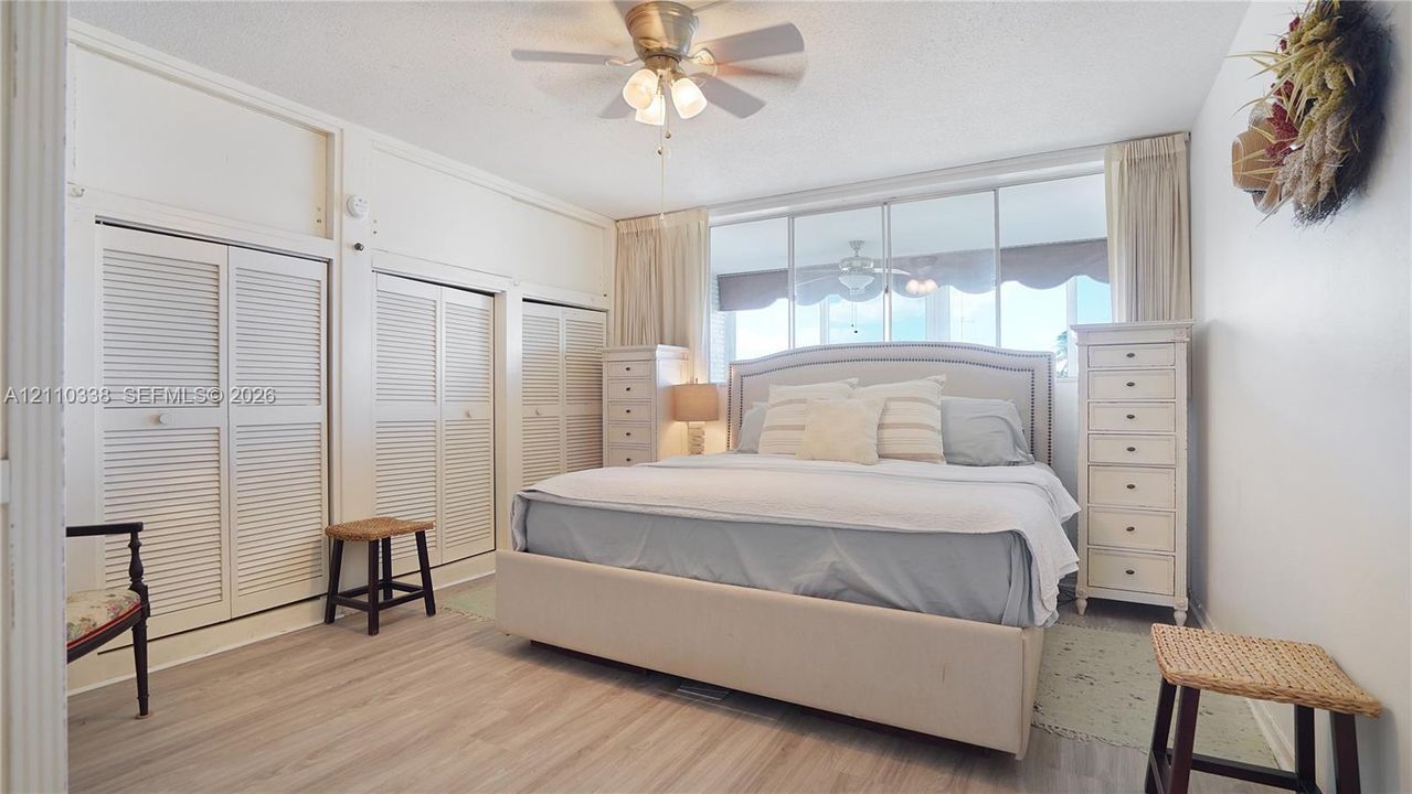Wood-finish flooring, multi-panel louvered closet doors, ceiling fan with integrated lighting, and expansive wall-to-wall glass windows WATER VIEWS!