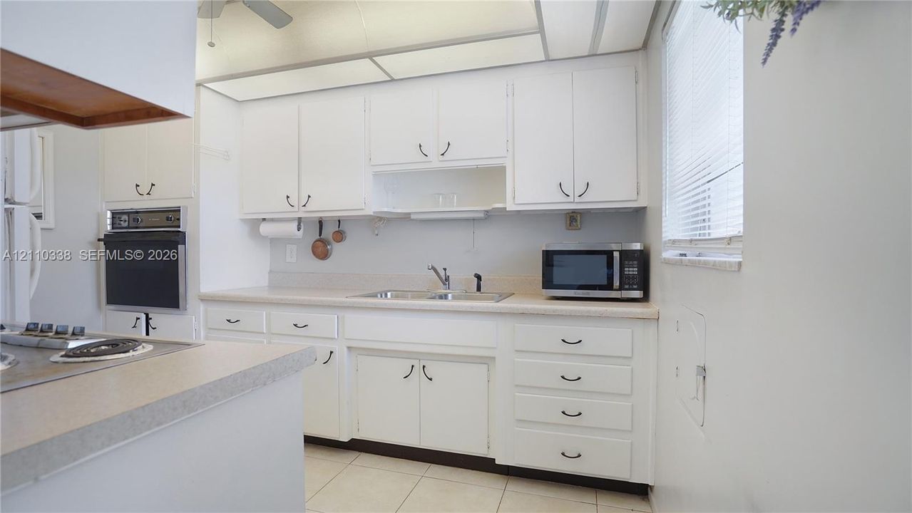 Kitchen featuring white cabinetry, integrated wall oven, laminate countertops, dual-basin sink with retractable faucet, and tile flooring