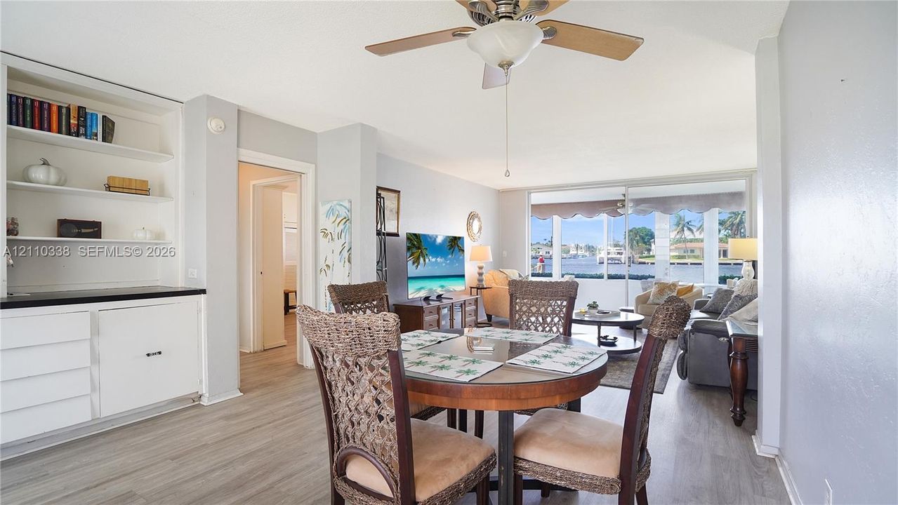 Living area featuring wood-finish flooring, floor-to-ceiling glass sliding doors, built-in shelving, white cabinetry with a stone-top surface, and a central ceiling fan