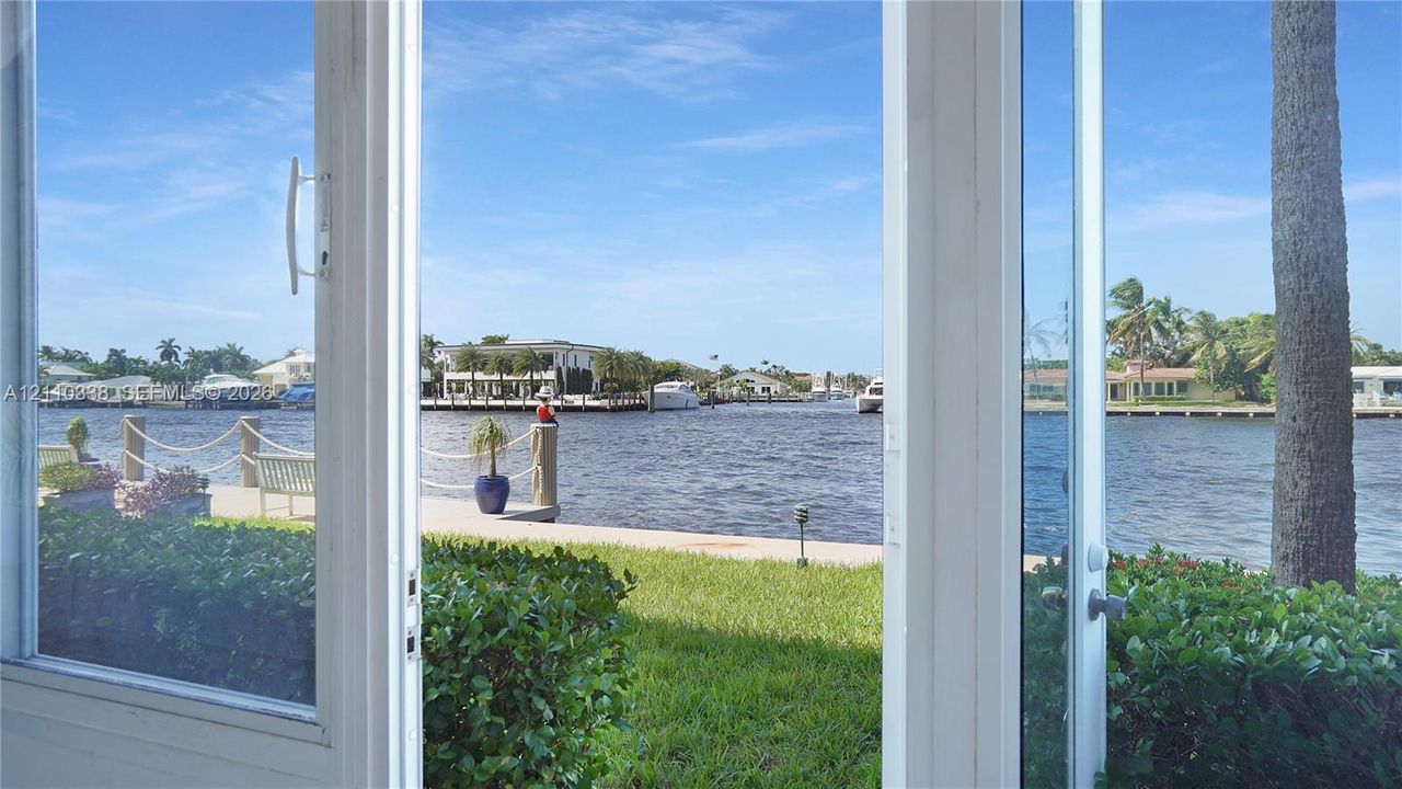 White-framed glass door system, concrete seawall, rope-railing dock, manicured lawn, and waterfront access