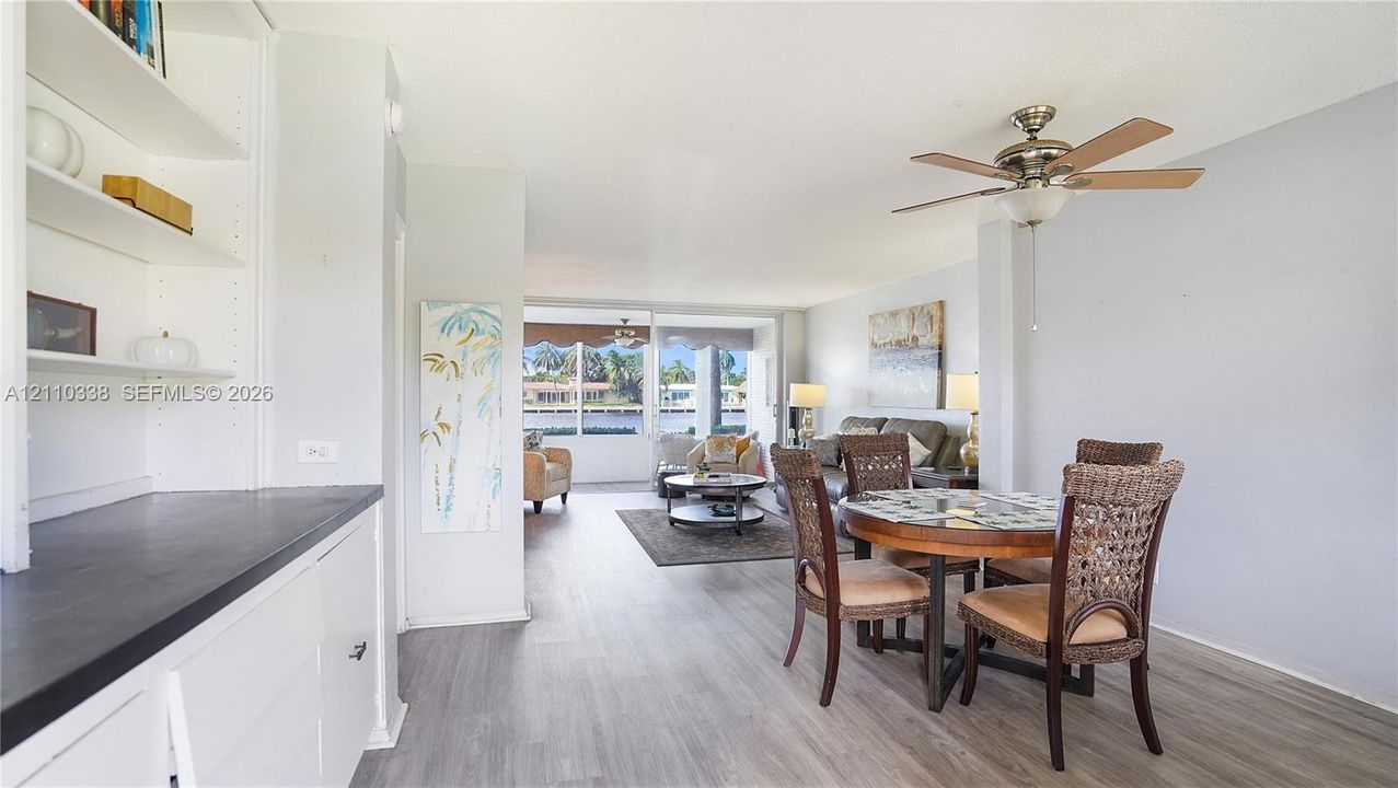 Open-concept floor plan featuring wood-finish flooring, built-in cabinetry with a dark countertop, a ceiling fan, and floor-to-ceiling windows