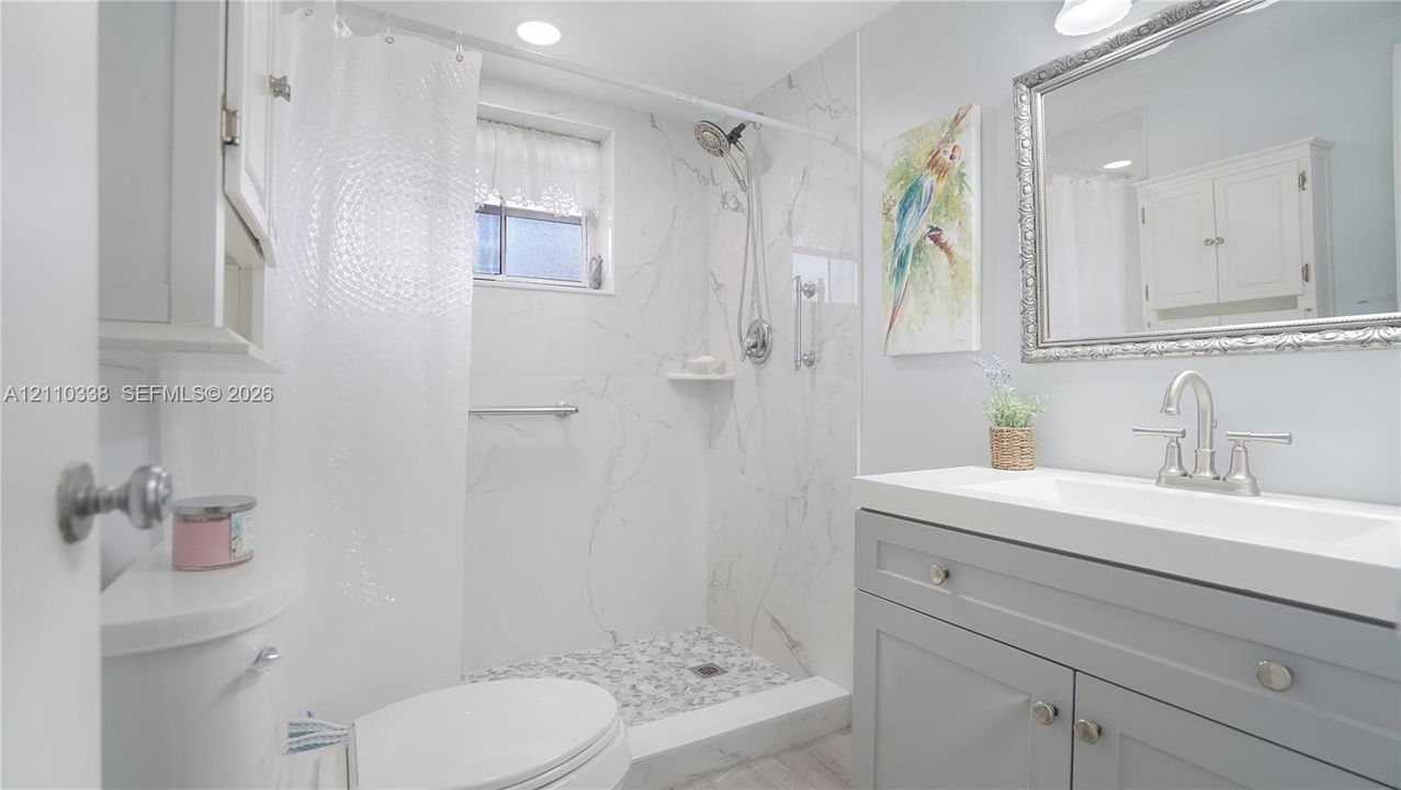 Walk-in shower with stone-finish surround and integrated shelving, grey vanity with rectangular basin, brushed-nickel widespread faucet, and rectangular mirror