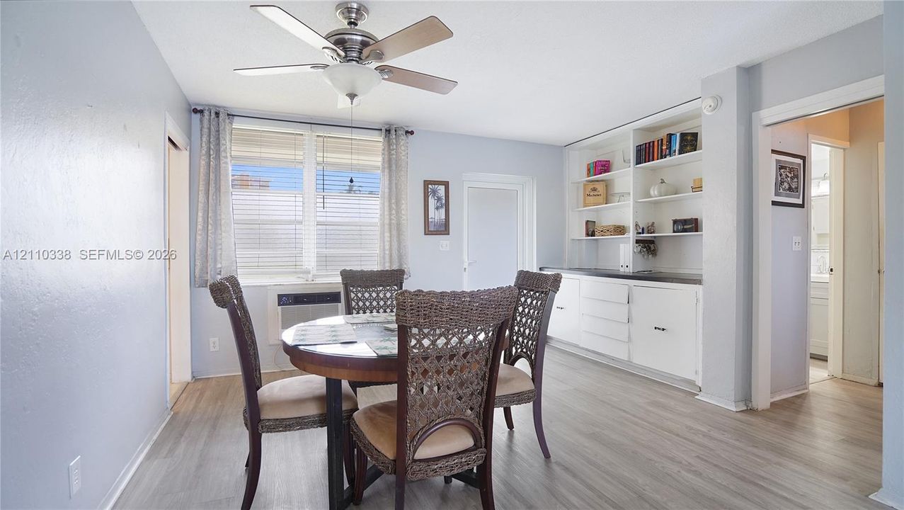 Dining area featuring wood-finish flooring, built-in white cabinetry with open shelving, and a central ceiling fan