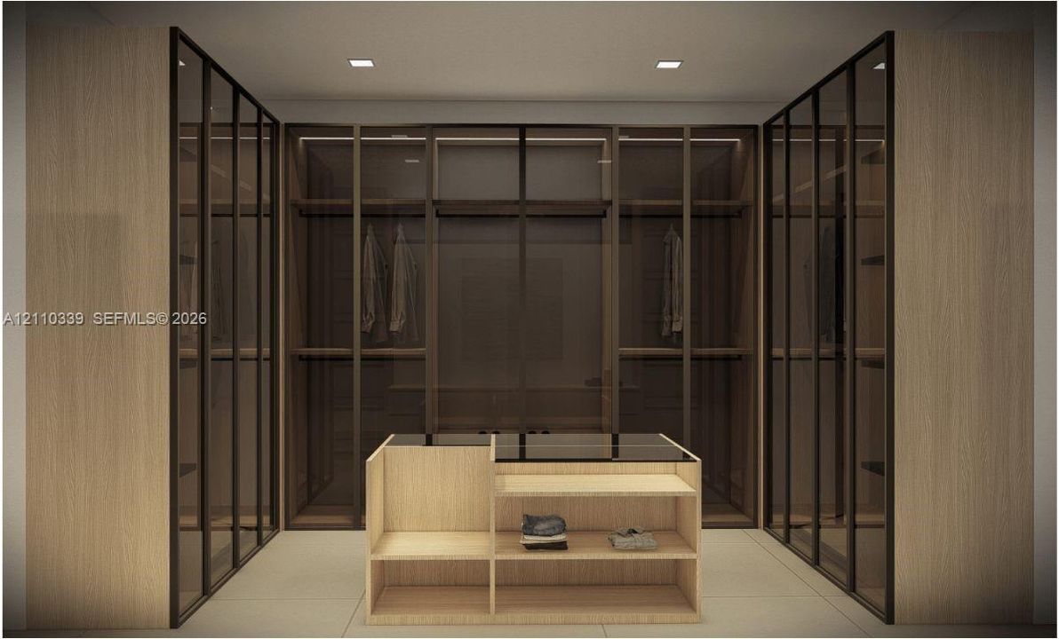 Custom dressing area featuring floor-to-ceiling cabinetry with glass-panel doors, integrated shelving, and a central built-in island with a countertop surface
