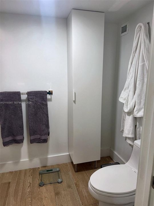 Full-height white storage cabinetry, wood-finish flooring, and a contemporary white toilet