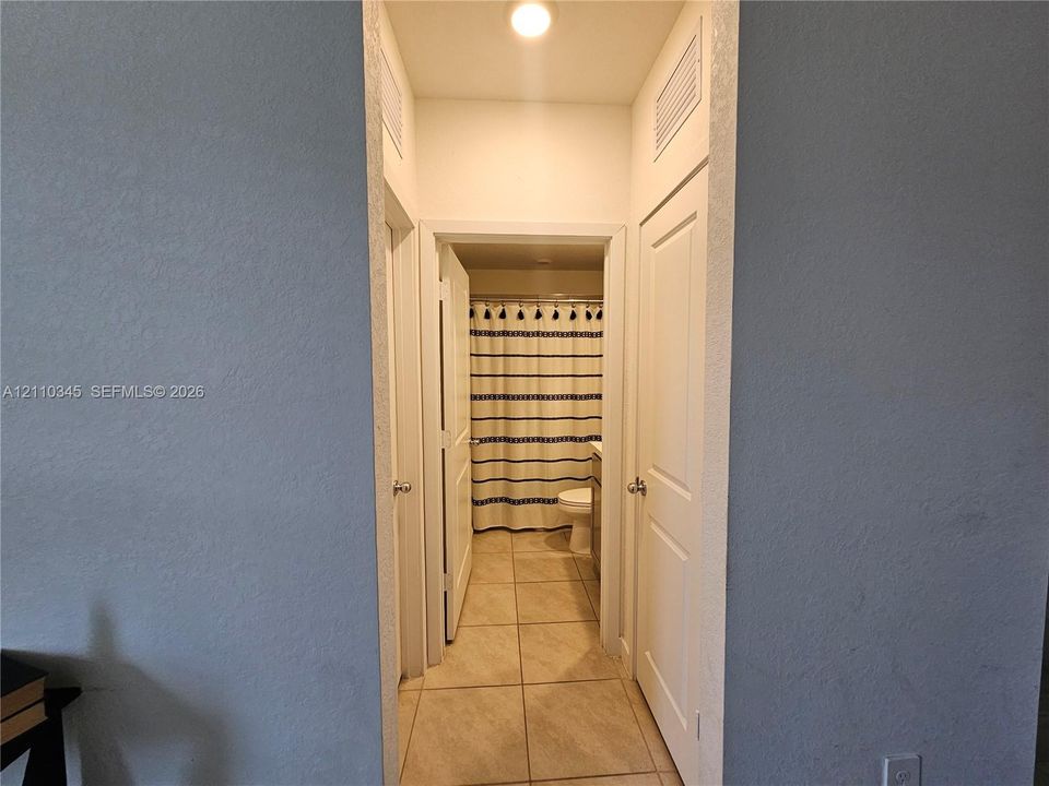 Hallway featuring tile flooring, neutral wall paint, and multiple interior doors with polished metal hardware