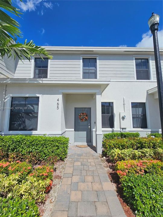 Two-story exterior featuring light-toned siding, a paved walkway, and manicured landscaping