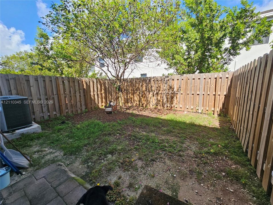 Fenced backyard featuring vertical wood-plank fencing, paver hardscaping, and mature trees