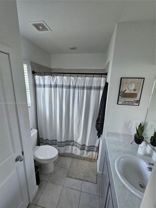 Bathroom featuring a single-sink vanity with a solid-surface countertop and a tile-surround shower combination