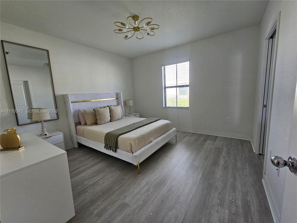 Bedroom featuring wood-finish flooring, a multi-arm metallic ceiling fixture, and a single-pane window with installed blinds
