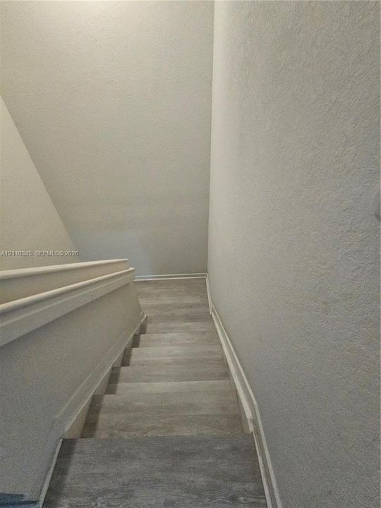 Staircase featuring wood-finish flooring and a painted wooden handrail