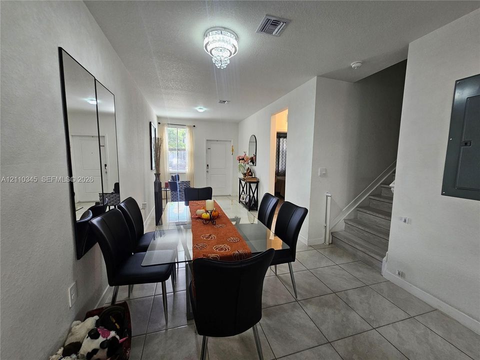 Neutral-toned floor tiling, wall-mounted mirrored paneling, recessed lighting, tiered crystal-style chandelier, and staircase with wood-finish treads