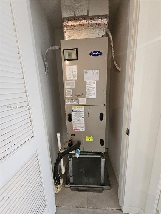 Carrier HVAC air handler unit featuring a metallic finish, mounted on a structural base, enclosed within a closet with louvered doors