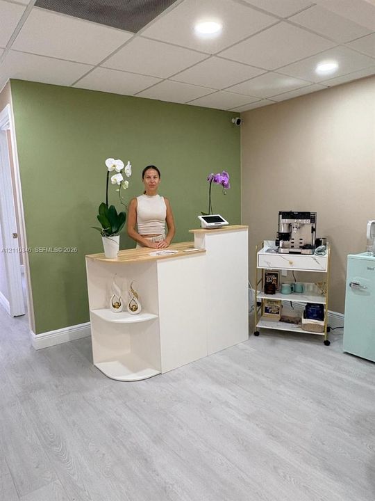 Reception area featuring a built-in white service desk with a light-toned wood-finish surface, recessed ceiling lighting, and wood-finish flooring