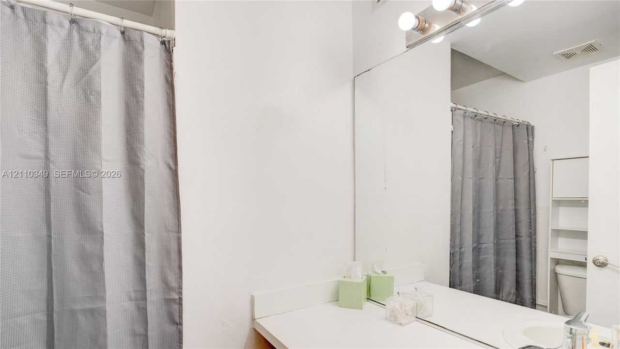 Bathroom featuring a full-width vanity mirror, a four-bulb vanity light fixture, and a built-in over-the-toilet storage unit