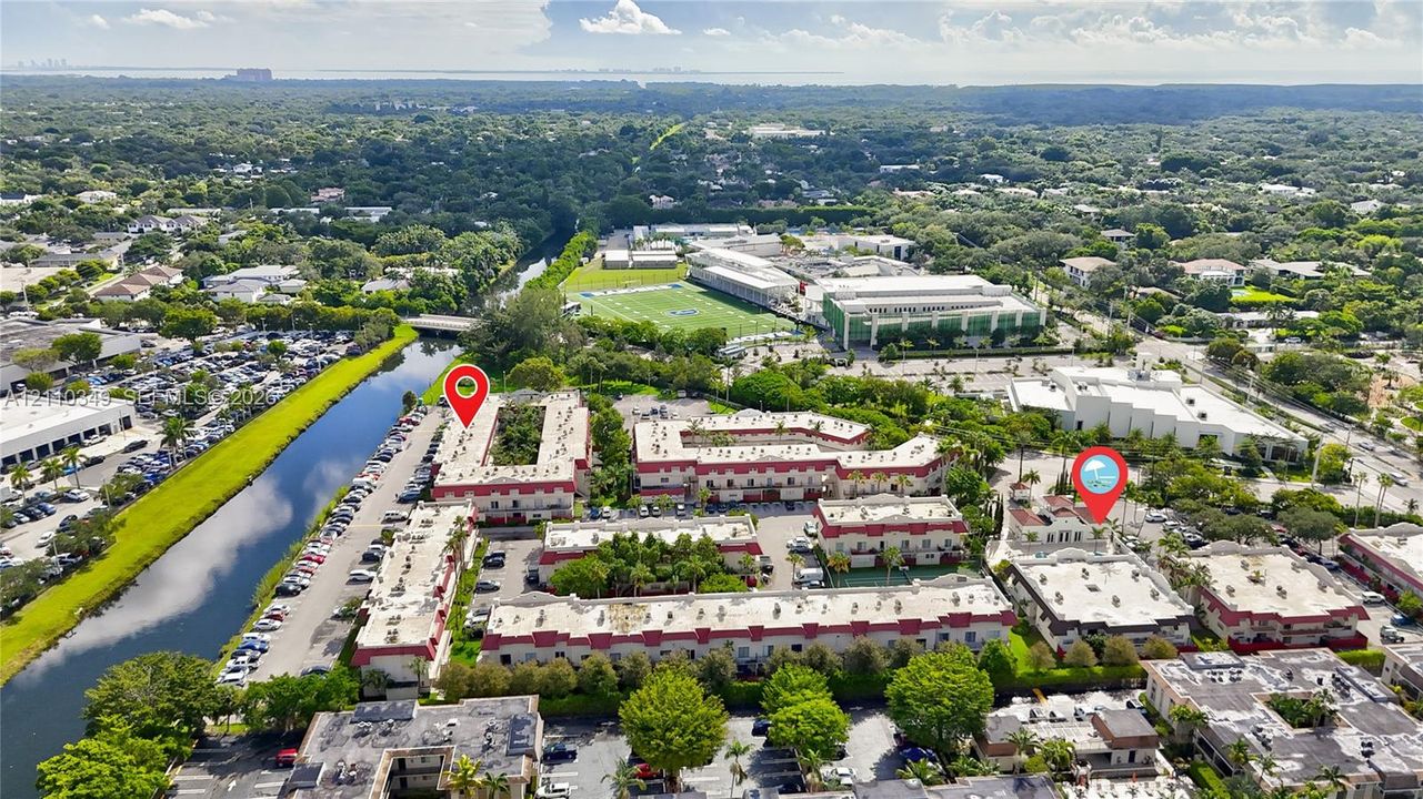 Aerial perspective of a multi-building residential complex featuring white stucco facades, terra cotta roof accents, mature landscaping, and an adjacent canal