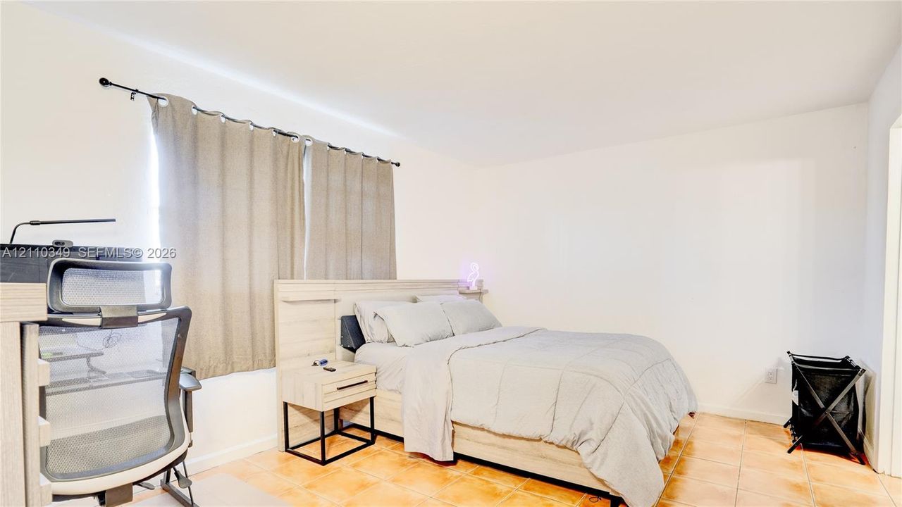Neutral-toned interior space featuring light-colored tile flooring, smooth white walls, and a window with a mounted curtain rod